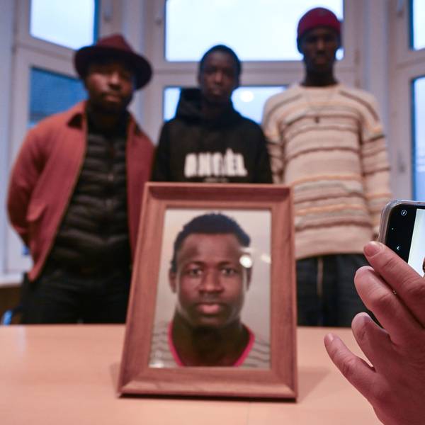 Sidy und Lassana Dramé stehen in den Räumen ihrer Rechtsanwältin hinter einem Foto ihres von Polizeischüssen getöteten Bruders Mouhamed Dramé.