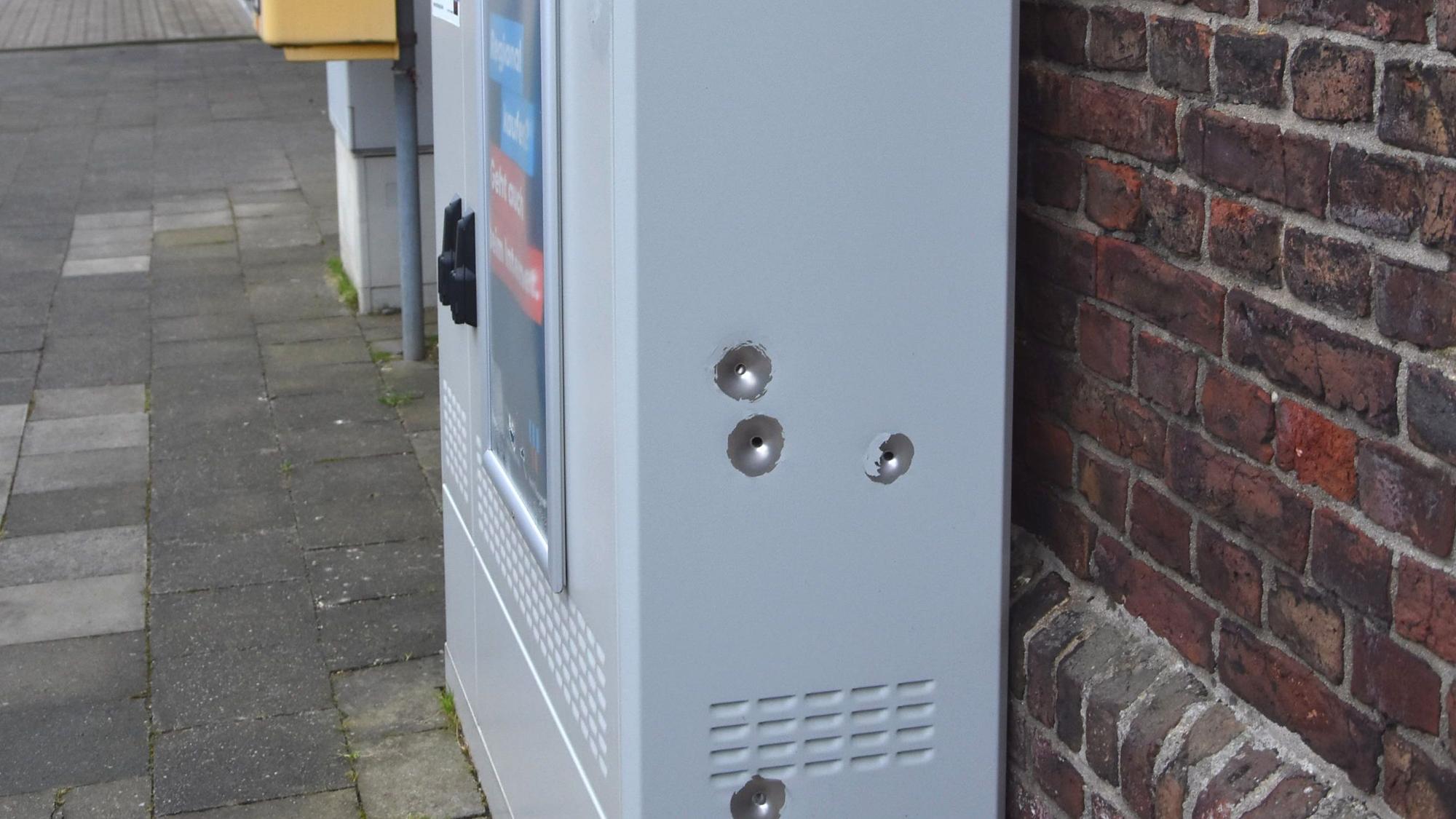 Auf dem Foto ist ein Glasfaser-Verteilerschrank zu sehen. An der Seite sind vier Einschusslöcher zu sehen.
