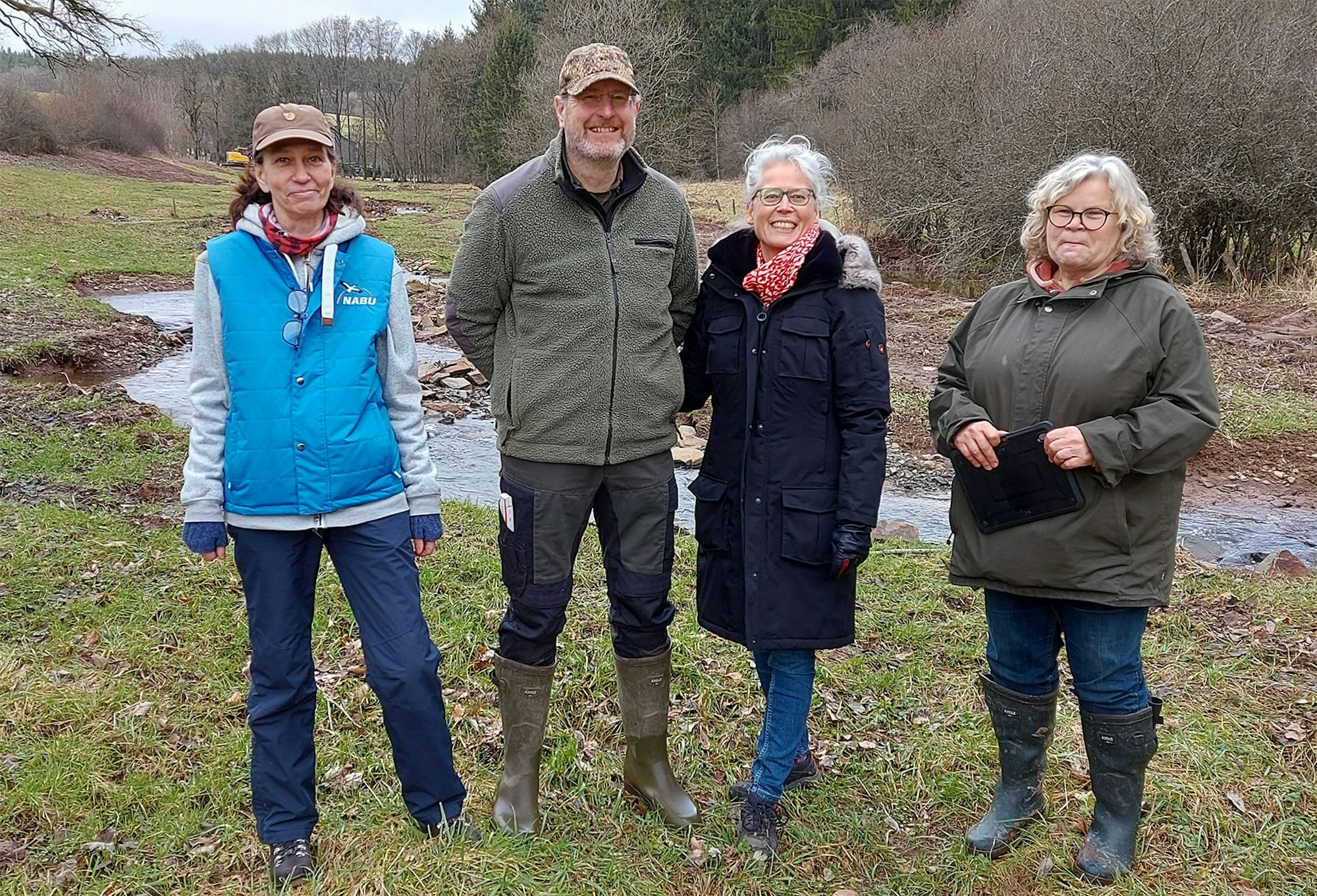 Ein Mann und drei Frauen stehen auf einer Wiese vor der renaturierten Berke.
