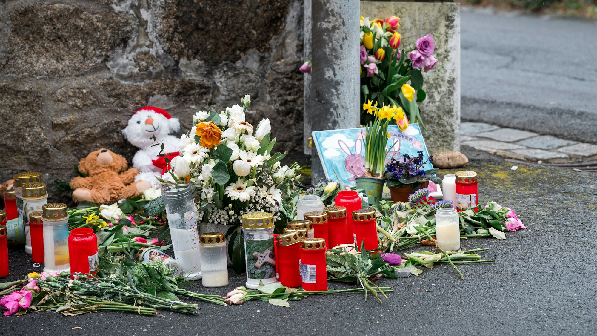 ARCHIV - 12.04.2023, Bayern, Wunsiedel: An einer Mauer vor dem Kinder- und Jugendhilfezentrum, in dem eine Zehnjährige tot aufgefunden wurde, liegen Blumen, Kuscheltiere und Kerzen. (zu dpa: «Welche bedeutenden Verfahren 2024 an Bayerns Gerichten anstehen») Foto: Daniel Vogl/dpa +++ dpa-Bildfunk +++
