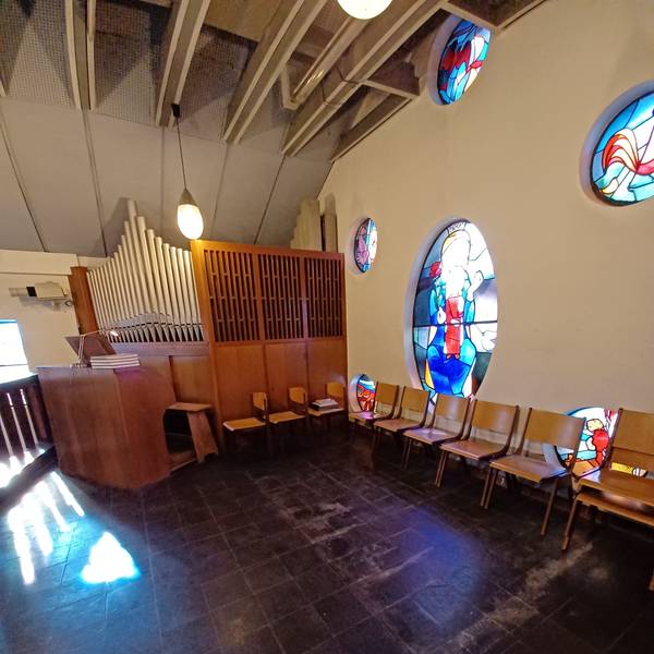Zu sehen ist die Orgel-Empore in einer Kirche, an einer Wand stehen Stühle.