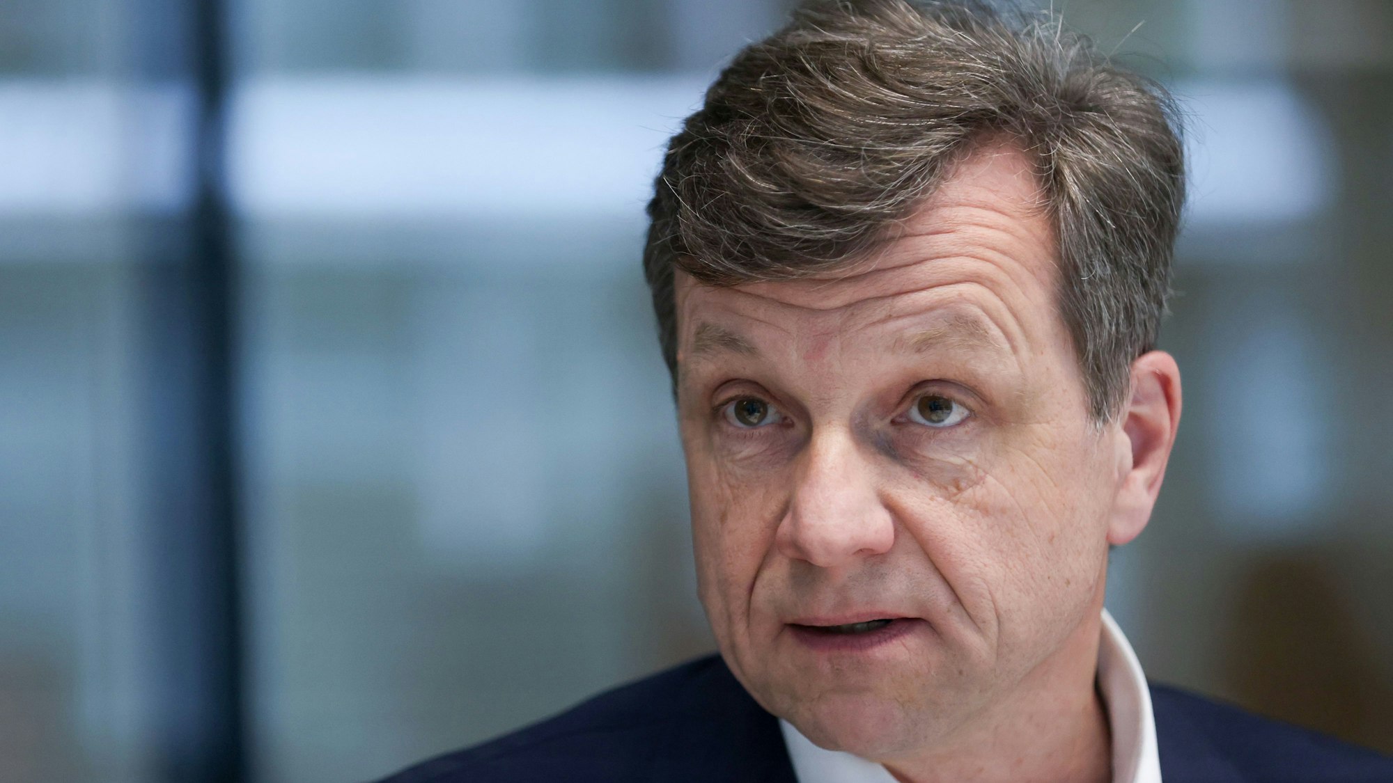 Porträtbild eines Mannes mit dunklem Haar und in dunklem Anzug ist zu sehen.