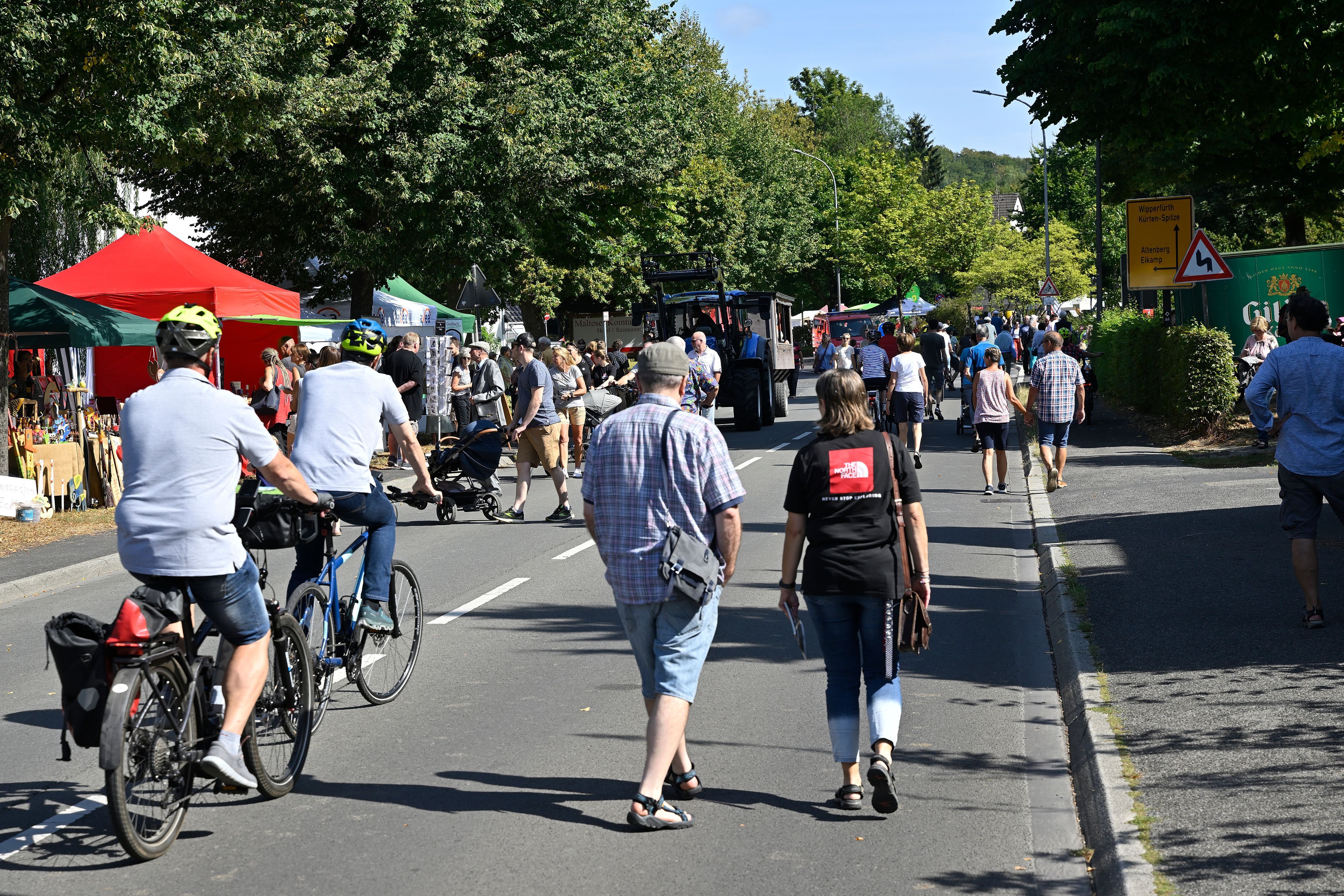 Zu sehen ist eine Straße, auf der Fußgänger schlendern und Fahrradfahrer unterwegs sind.