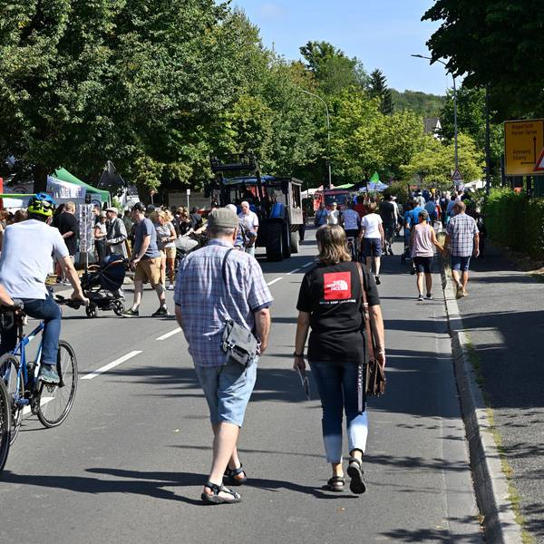 Zu sehen ist eine Straße, auf der Fußgänger schlendern und Fahrradfahrer unterwegs sind.