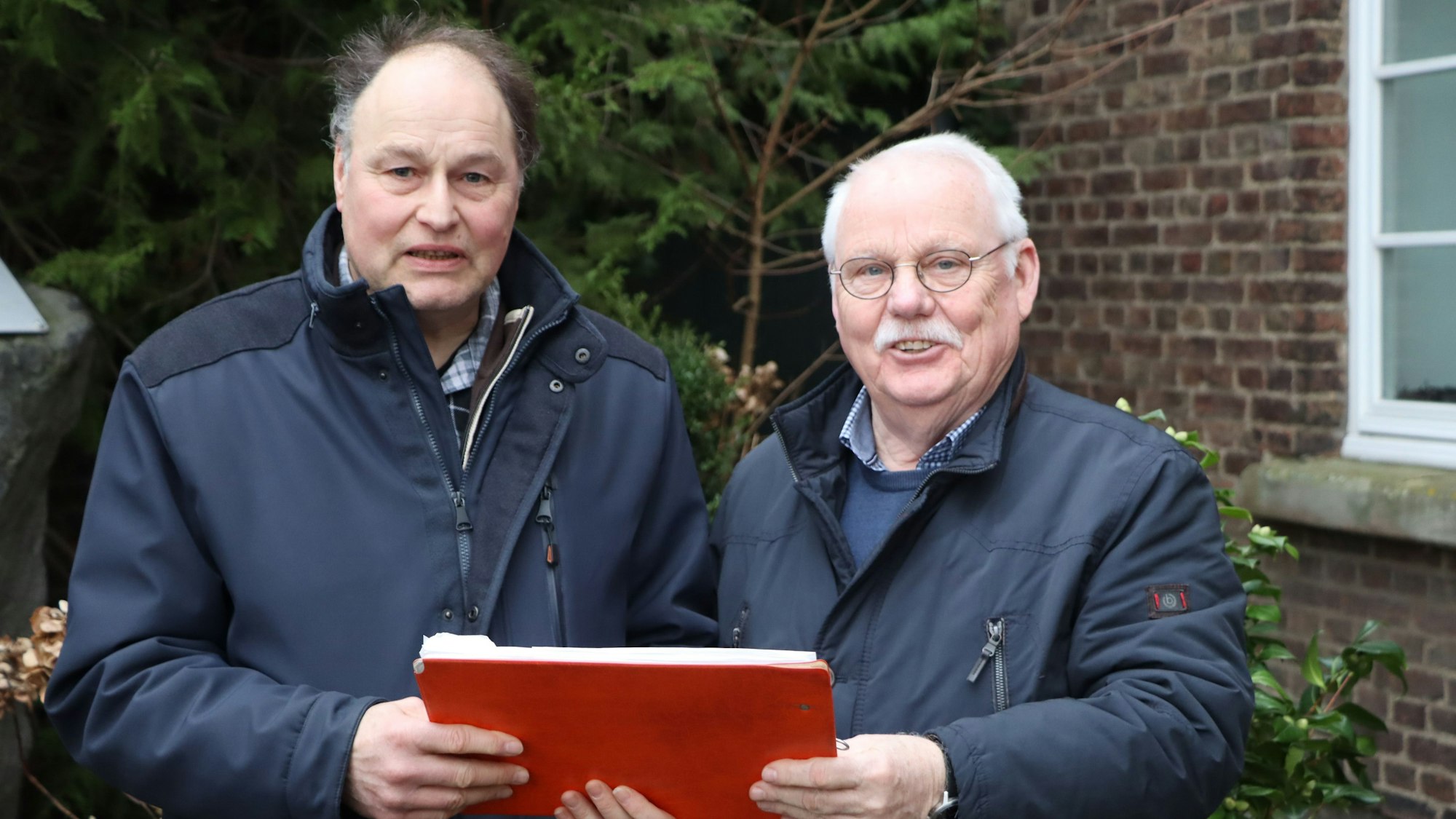 Zwei Männer halten ein Heft in den Händen und lächeln.