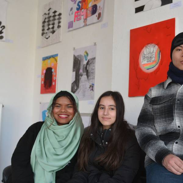 Schülerinnen und Schüler der Klasse EF der Gesamtschule Euskirchen sitzen vor ihren Bildern zum Thema „Gesicht zeigen“ in der Galerie FzKKE.