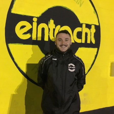 Ömer Tokac im Porträt vor einer gelben Wand mit schwarzem Eintracht-Schriftzug.
