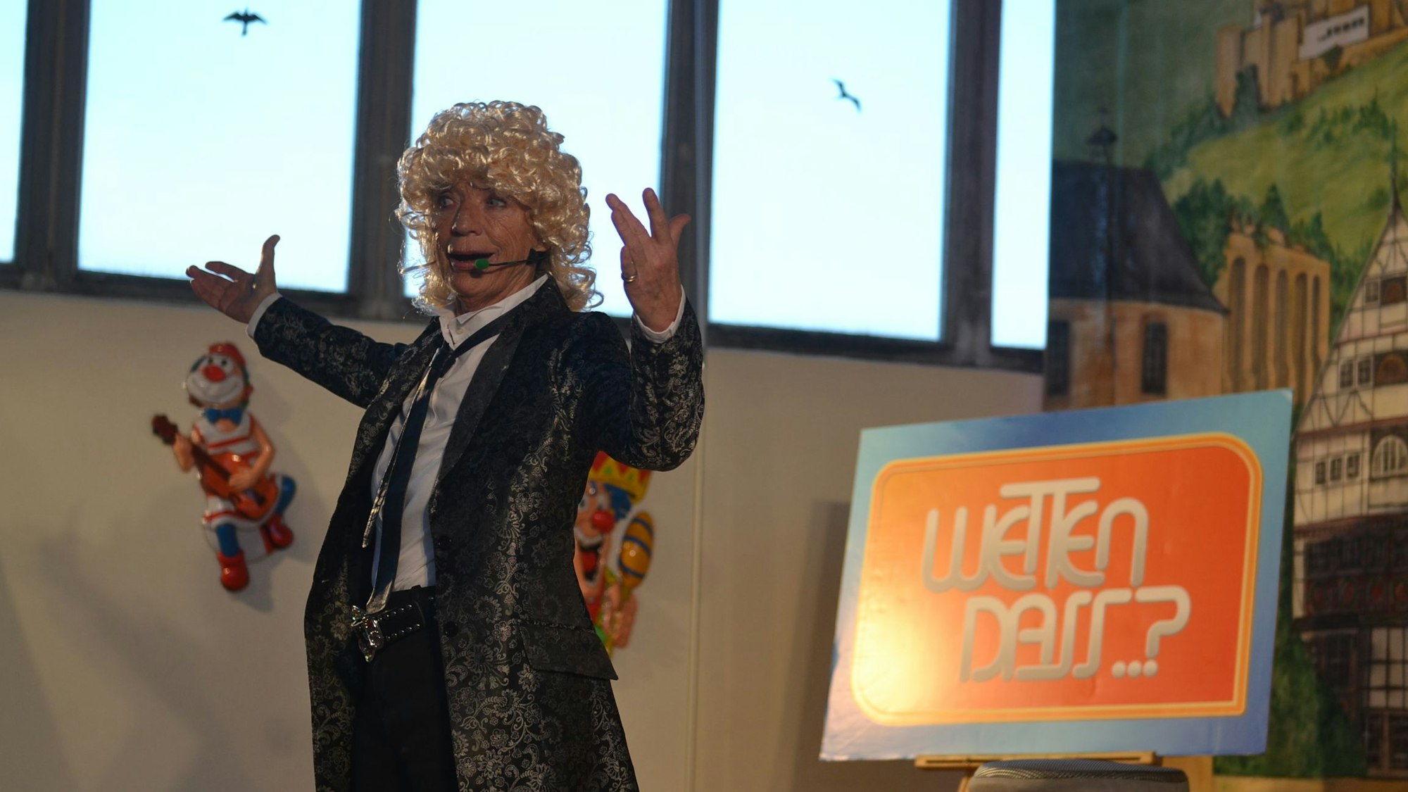 Sylvie Meiser steht als Thomas Gottschalk verkleidet auf einer Bühne,