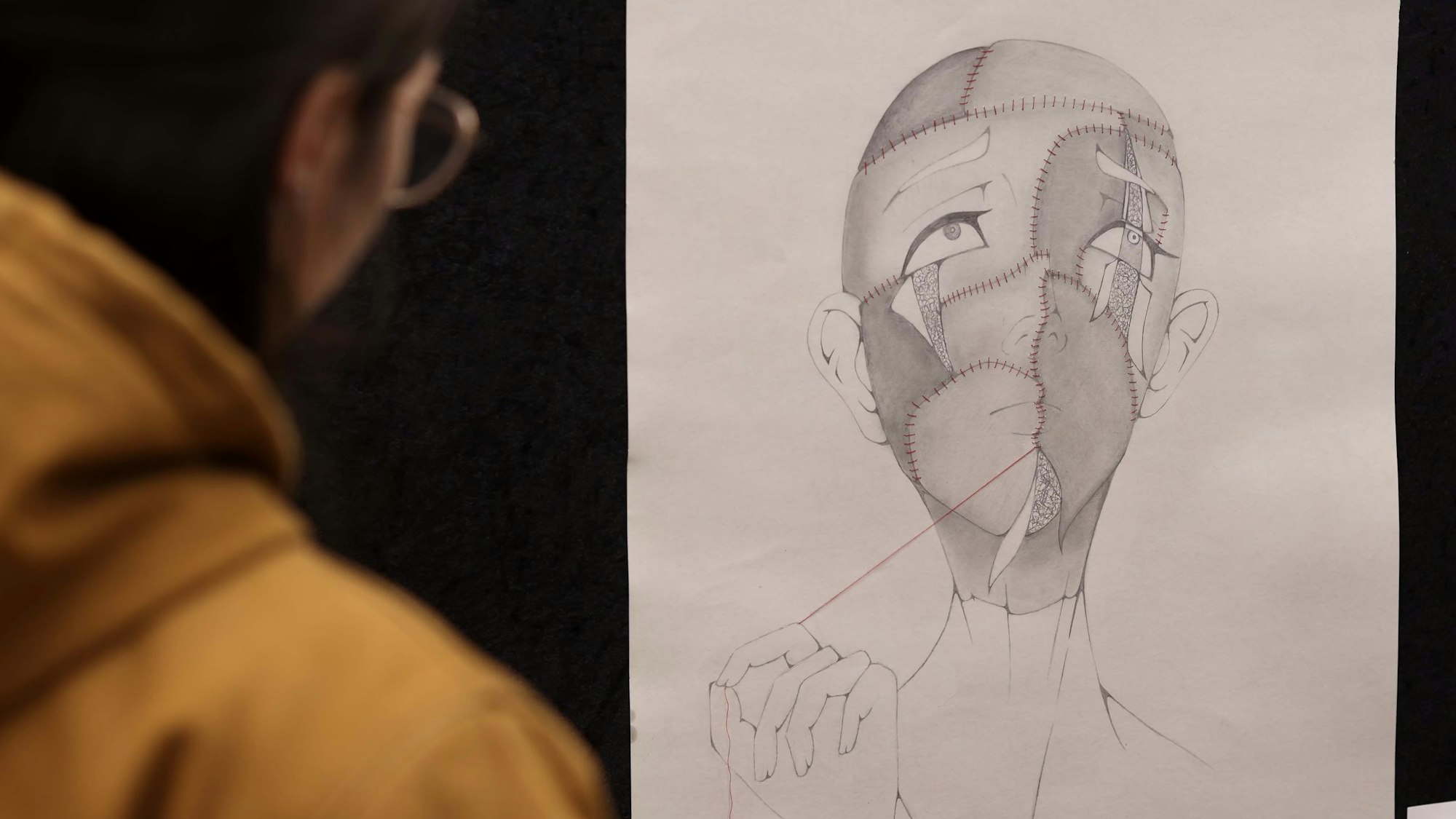 Mit Nadel und Faden wird auf einer Zeichnung ein Gesicht mühsam zusammengenäht.