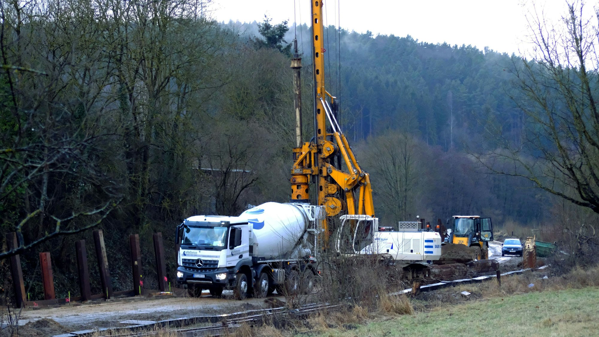 Bauarbeiten zum Wiederaufbau der Eifelstrecke im Urfttal bei Sötenich. Ein Betonmischer und andere Baumaschinen stehen auf der Eisenbahntrasse.