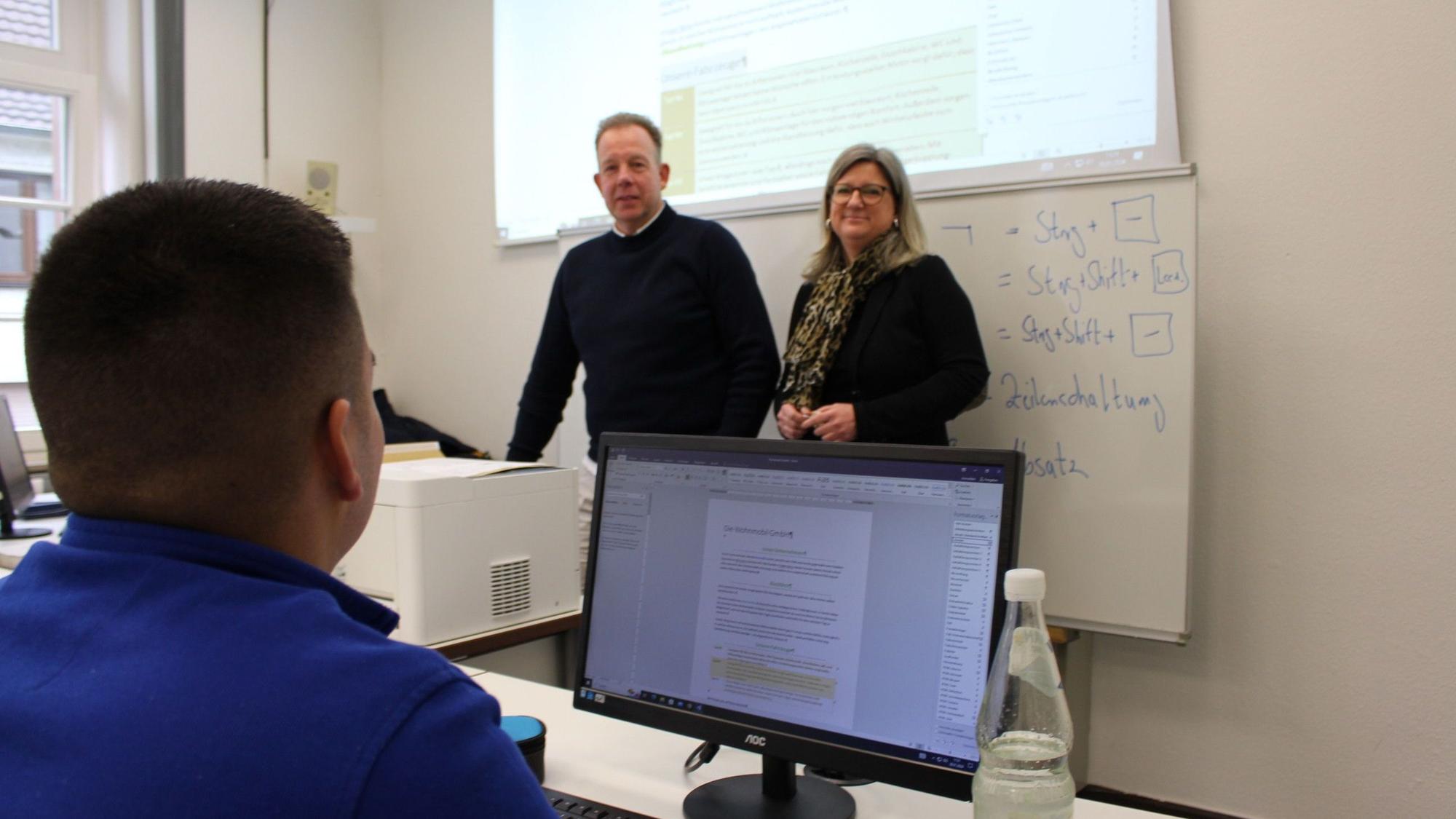 Vanessa Becker, Leiterin der Volkshochschule des Kreises Euskirchen, steht neben einem Kursleiter. Im Vordergrund sitzt ein Teilnehmer hinter einem Computerbildschirm.