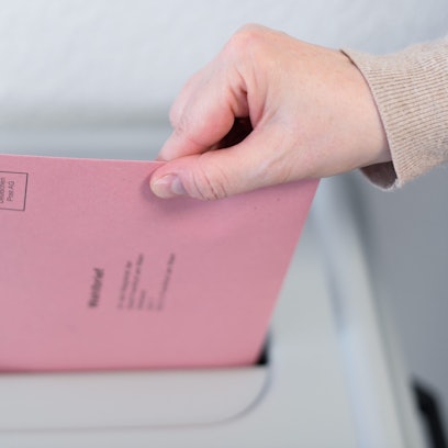 Eine Frau wirft ihren Wahlbrief in eine Wahlurne.