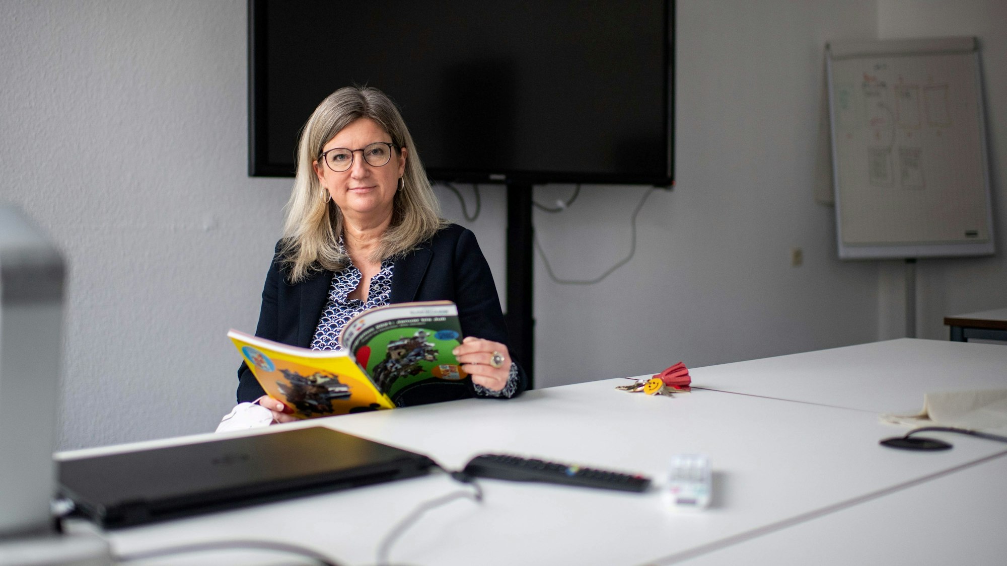 Vanessa Becker sitz an einem Tisch mit einem aufgeschlagenen Programm der VHS. Sie schaut in die Kamera.