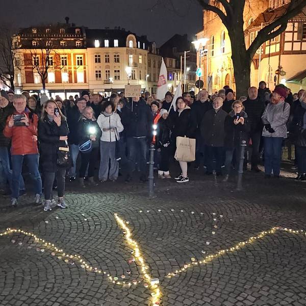 Menschen stehen auf dem Konrad-Adenauer-Platz von Bergisch Gladbach, auf dem Boden ist ein leuchtendes Peace-Zeichen zu sehen.