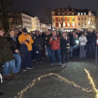 Menschen stehen auf dem Konrad-Adenauer-Platz von Bergisch Gladbach, auf dem Boden ist ein leuchtendes Peace-Zeichen zu sehen.