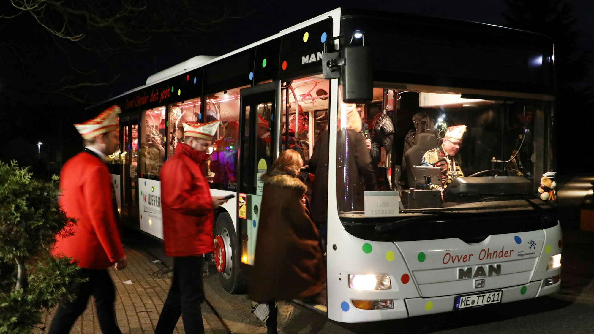 Menschen steigen bei Dunkelheit in einen erleuchteten Linienbus ein.