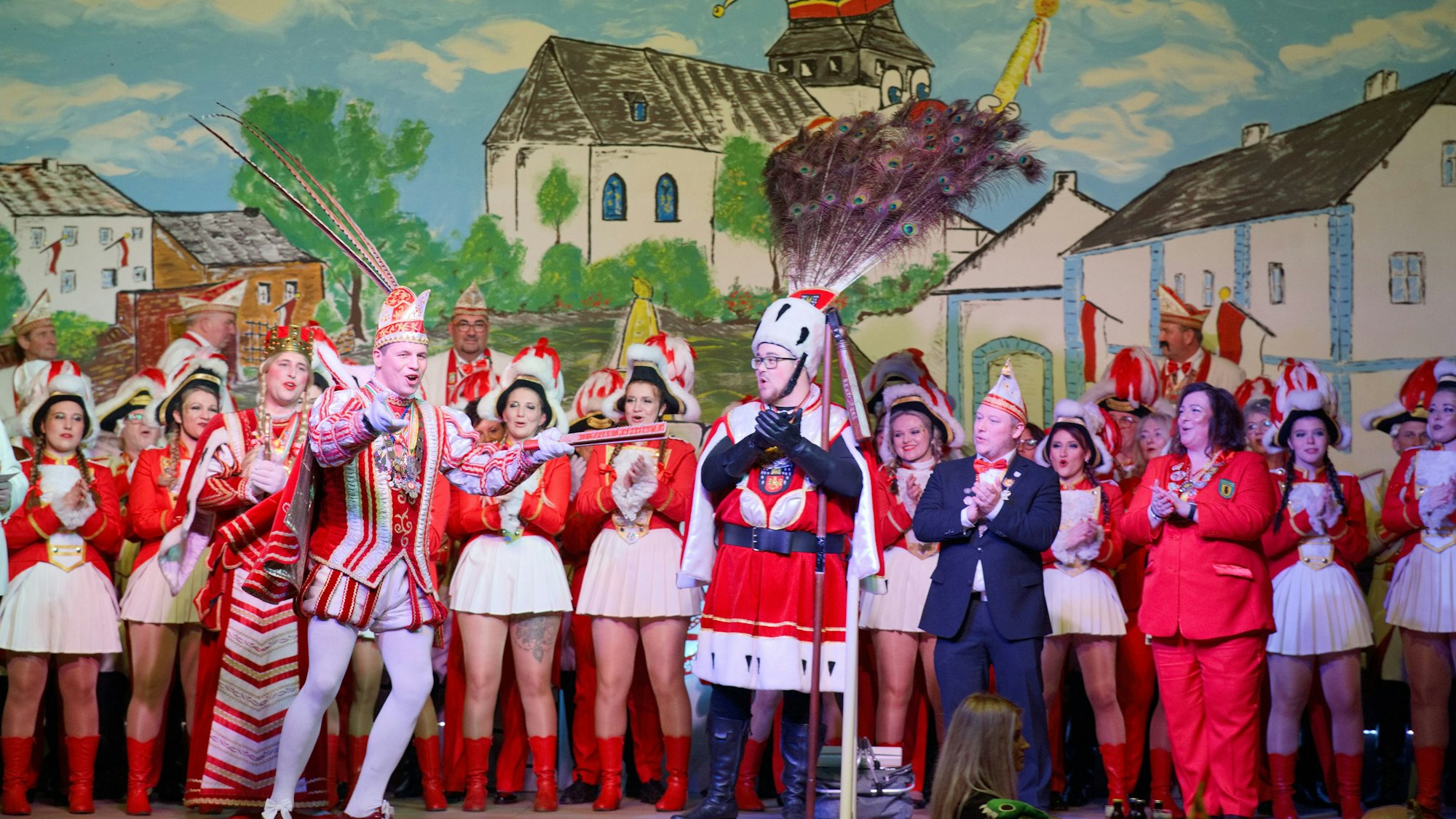 Prinz Hubertus Bollig, Bauer Paul Esser und Jungfrau Tobias Kohlenbaum stehen mit weiteren Karnevalisten vor dem Bühnenbild.