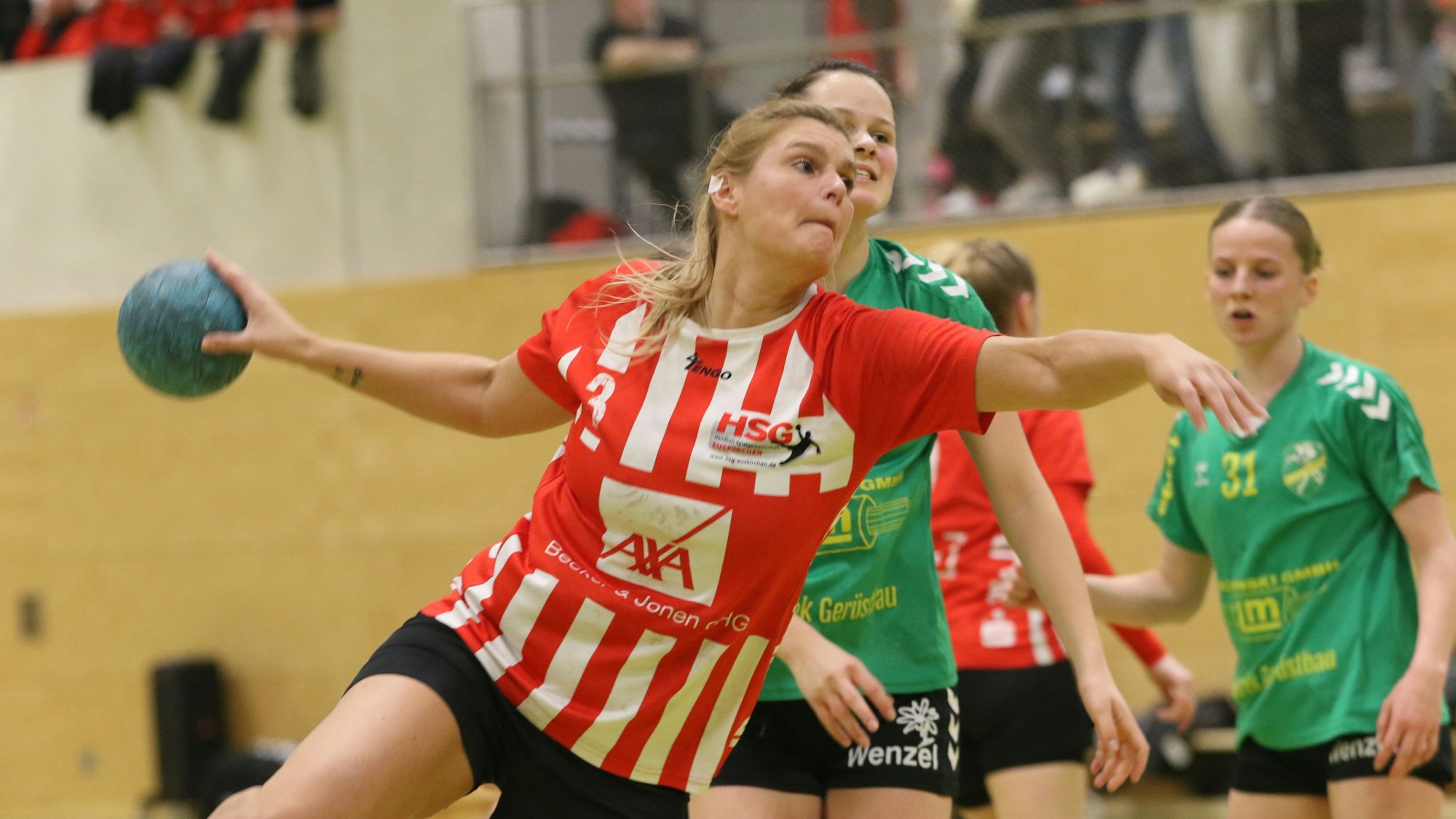 Sabine Schmitz springt mit Willen und Zuversicht zum Torwurf. Ihr Ohr-Piercing ist abgeklebt. Den blauen Ball streckt sie vom Körper weg, um auszuholen.