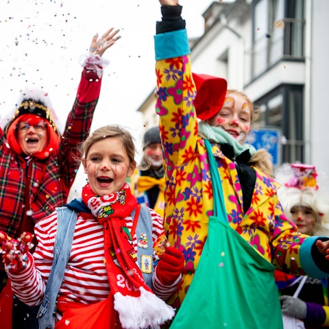 Das Bild zeigt drei Jecke während des Kinderzugs. Die haben gerade Konfetti in die Luft geworfen.