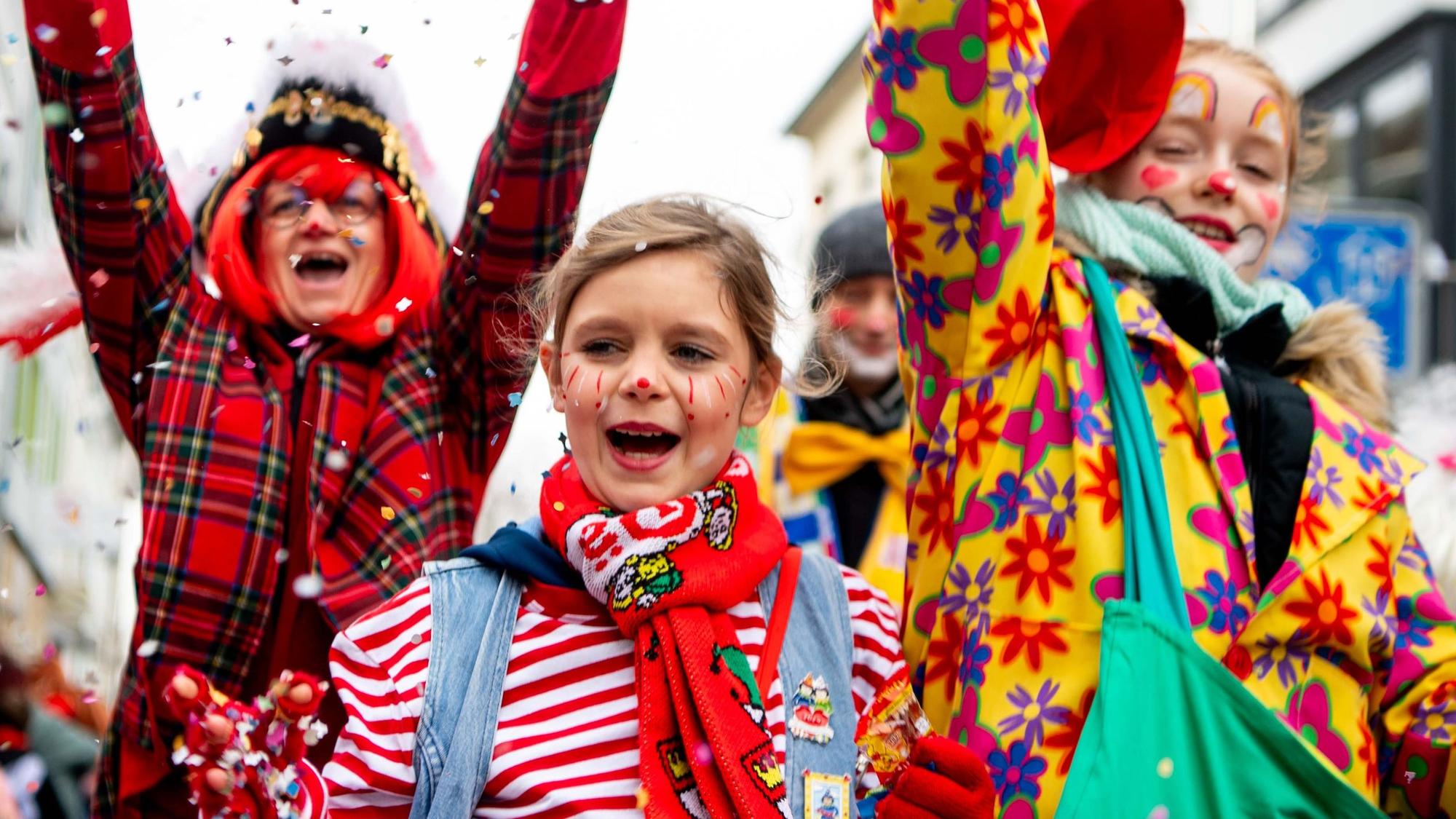 Das Bild zeigt drei Jecke während des Kinderzugs. Die haben gerade Konfetti in die Luft geworfen.