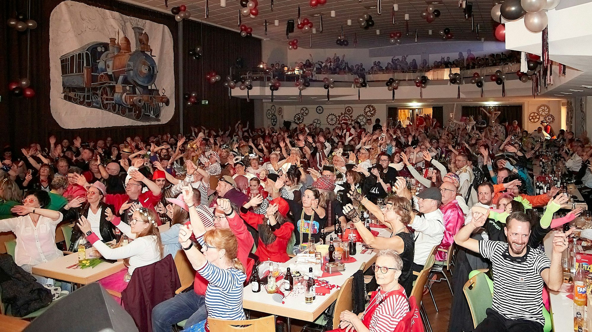 Kostümierte Karnevalisten feiern im mit Luftballons dekorierten Saal.