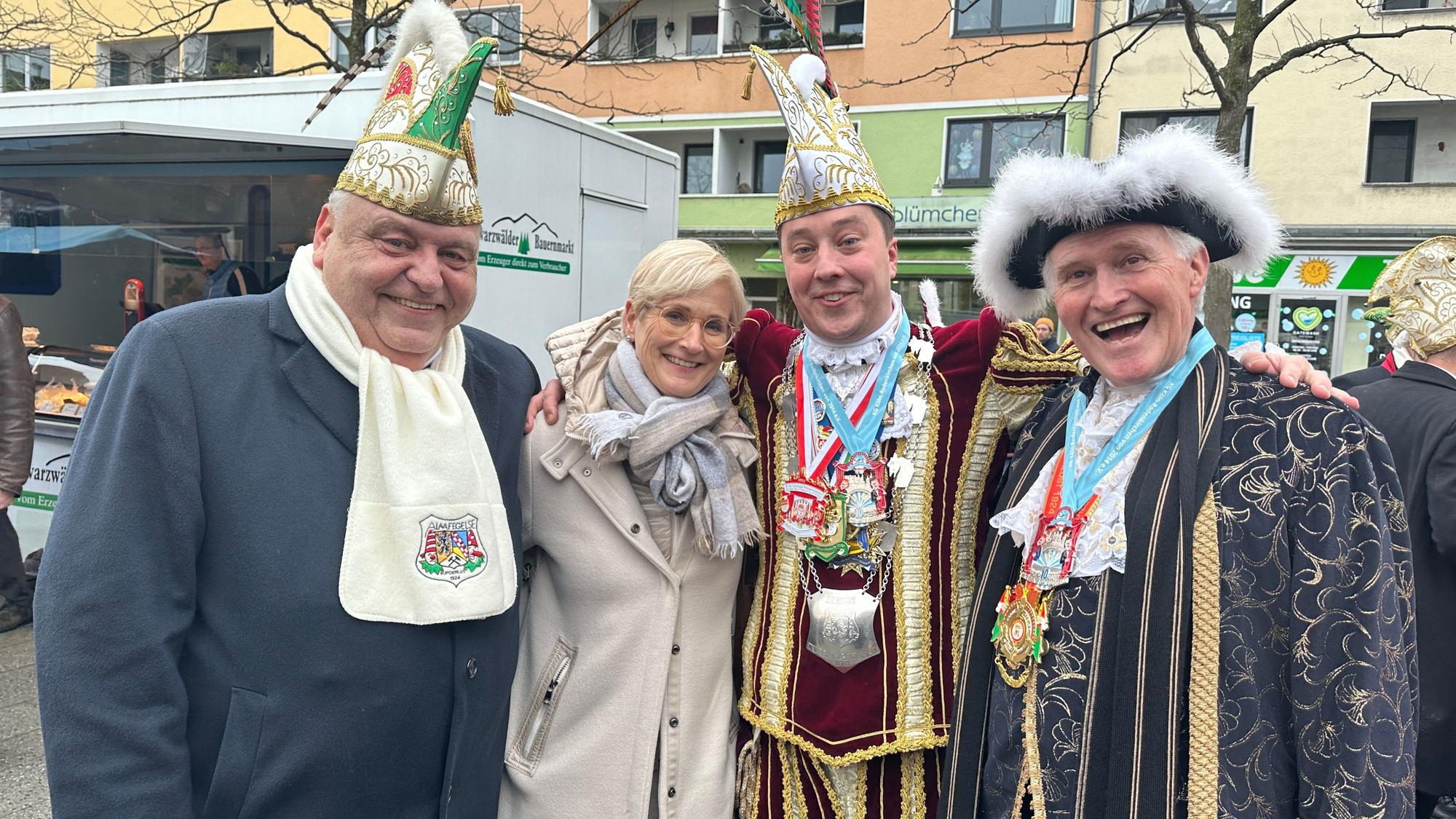 Drei Herren in Kostümen und eine unkostümierte Frau stehen nebeneinander.