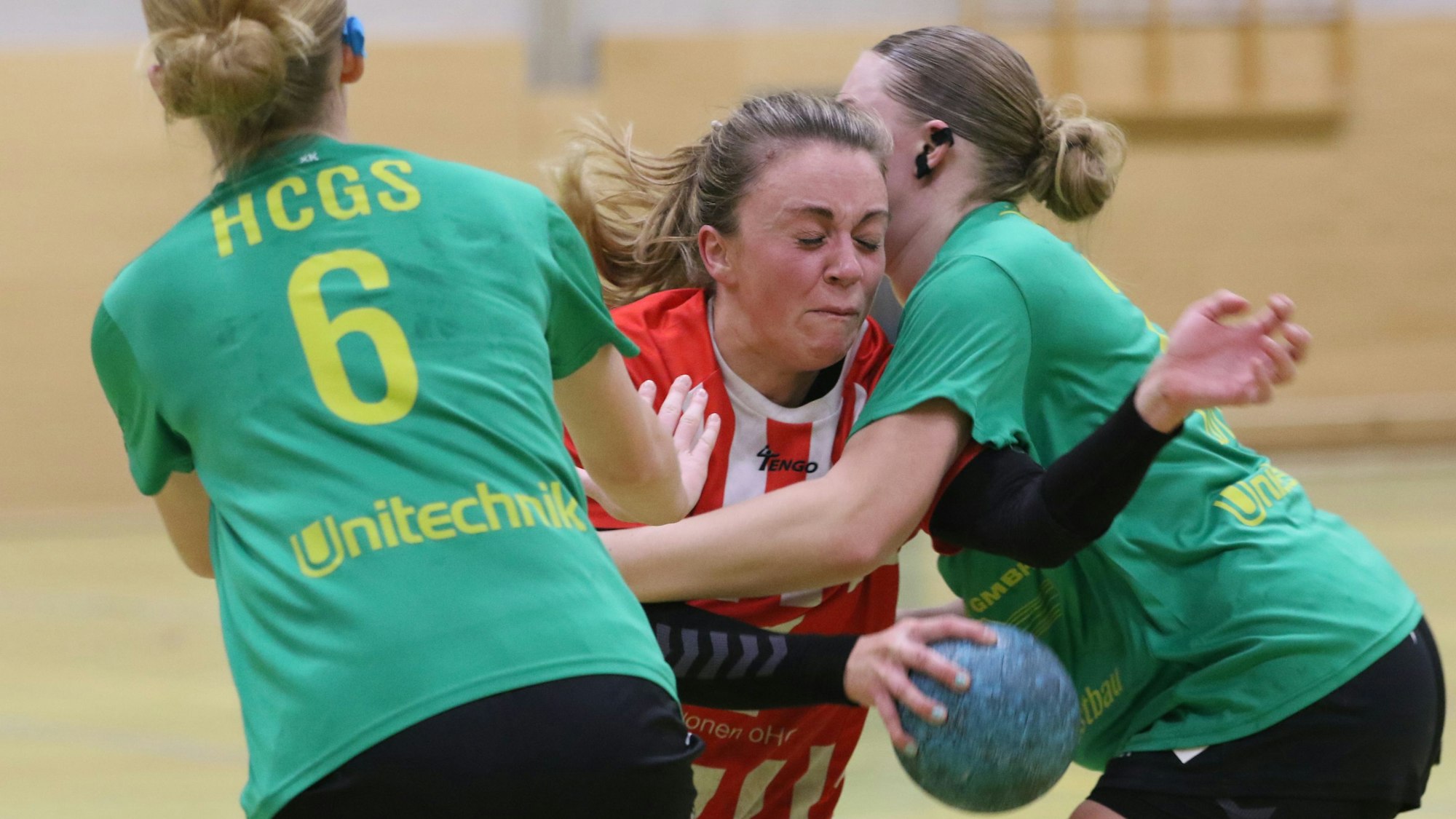 Svenja Bank wird von zwei Gegenspielerinnen rigoros gestoppt. Die eine streckt die Hand aus, die andere hat sie im Klammergriff. Bank hält den Ball in der Hand und hat die Augen geschlossen.