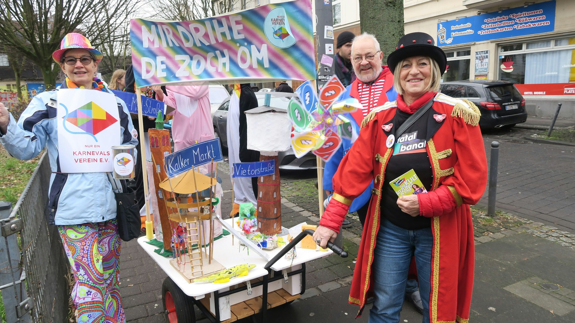 Neben einem Handwagen mit selbstgebastelten Aufbauten stehen zwei verkleidete Frauen und ein Mann.