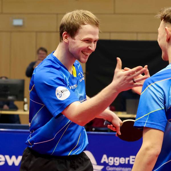 Die beiden Tischtennisspieler Benedikt Duda und Adrien Rassenfosse lachen und schlagen mit den Händen ein.