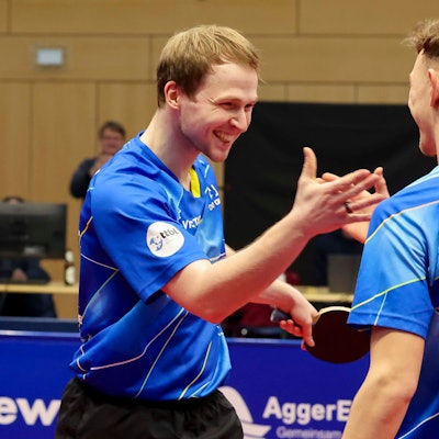 Die beiden Tischtennisspieler Benedikt Duda und Adrien Rassenfosse lachen und schlagen mit den Händen ein.
