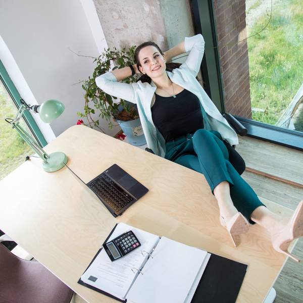 Eine Frau legt die Beine auf den Bürotisch und sieht entspannt aus.