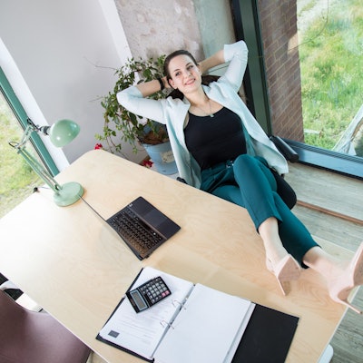 Eine Frau legt die Beine auf den Bürotisch und sieht entspannt aus.