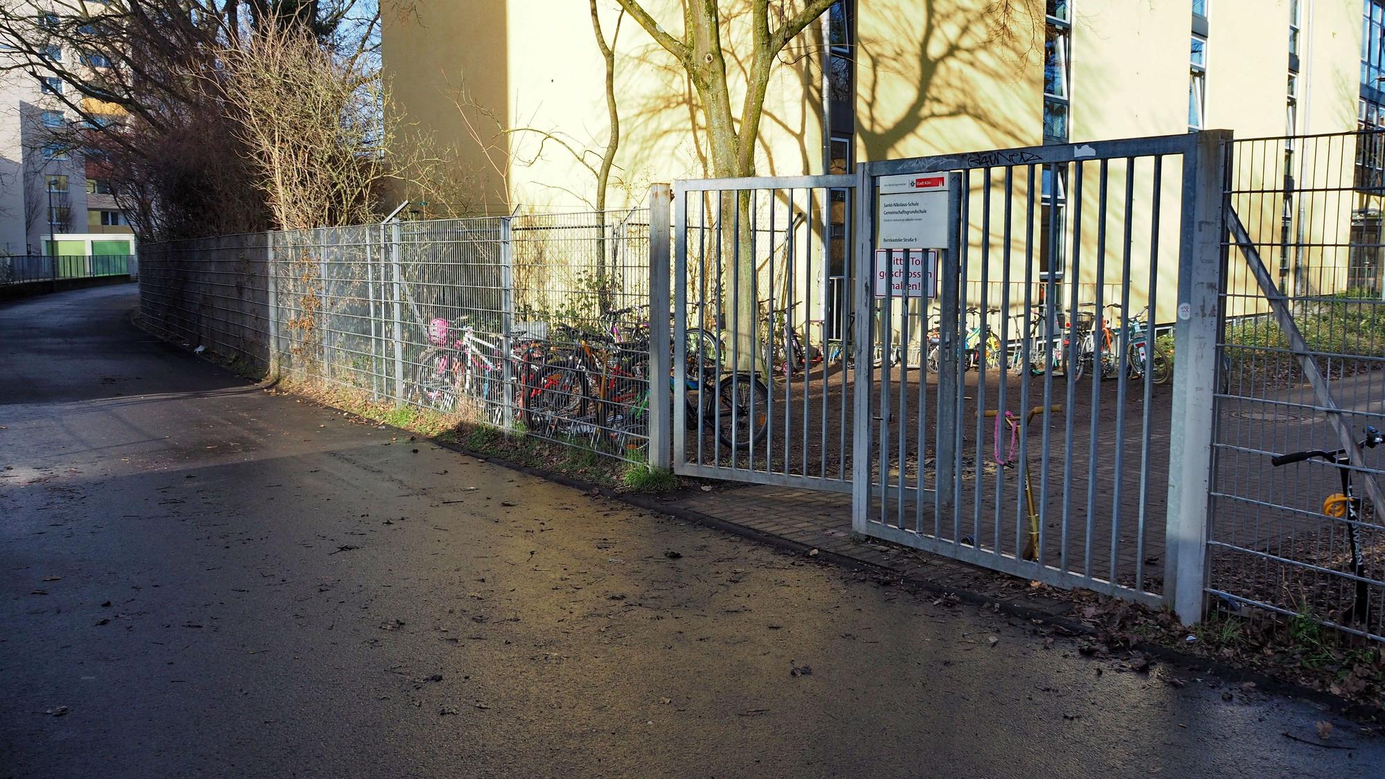 An einem Tor zu einem Schulgelände führt ein breiter Weg entlang.