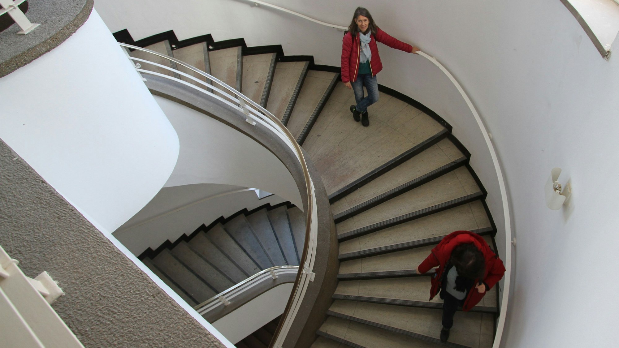 Zwei Frauen lauen eine gewundene Treppe herunter.
