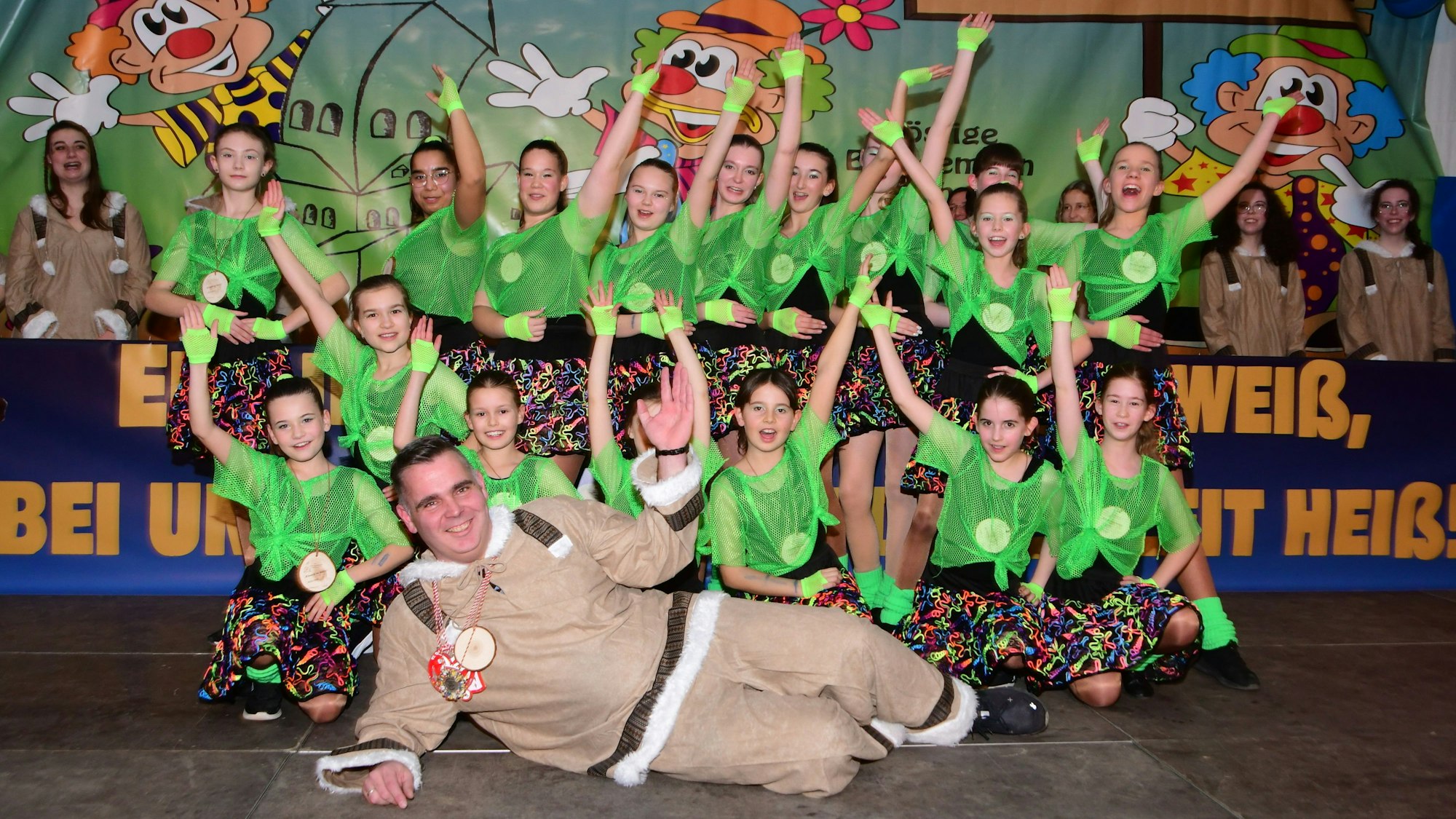 Eine Tanzgruppe steht auf der Bühne, der Präsident der Karnevalssitzung liegt vor ihnen.