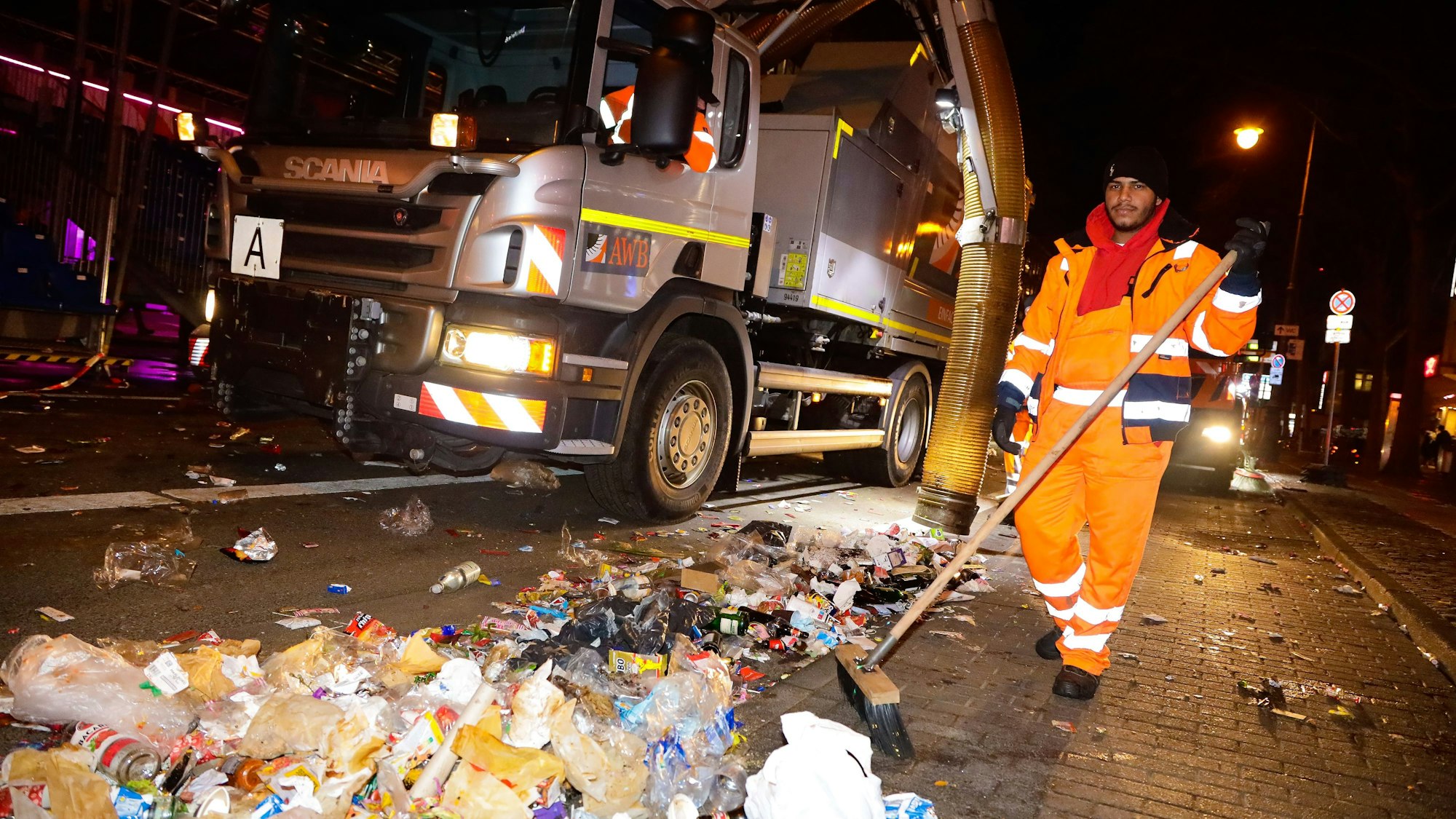 Ein Mitarbeiter der AWB beseitigt Müll am Straßenrand. Neben ihm steht ein Reinigungsfahrzeug.