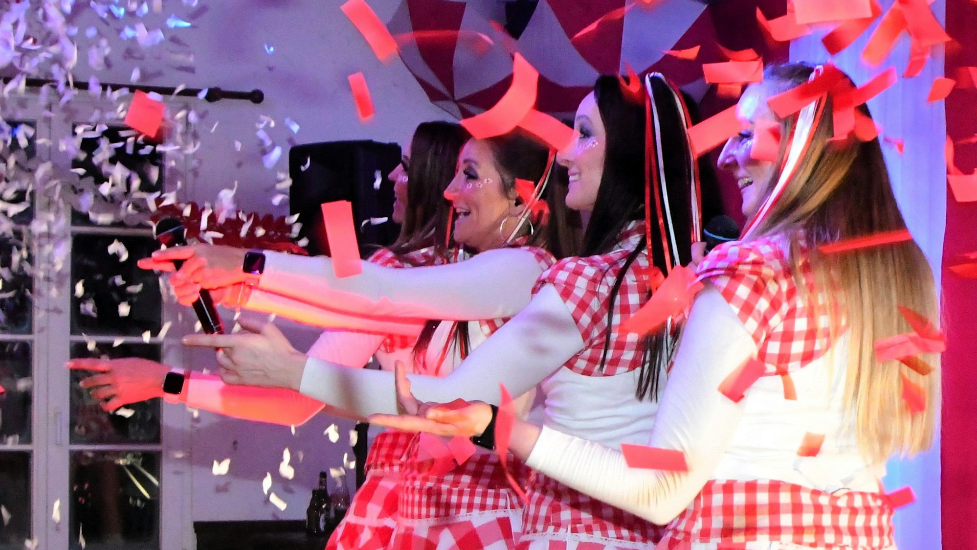 Die Funky Marys stehen hintereinander auf der Bühne, den linken Arm ausgestreckt. Papierschnipsel in Rot und Weiß fliegen über die Bühne.