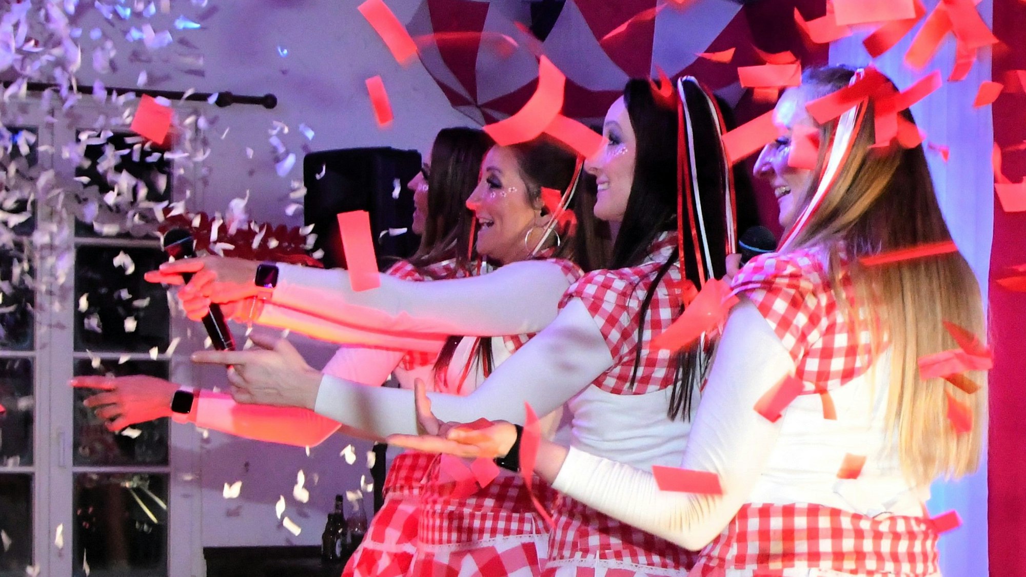 Die Funky Marys stehen hintereinander auf der Bühne, den linken Arm ausgestreckt. Papierschnipsel in Rot und Weiß fliegen über die Bühne.