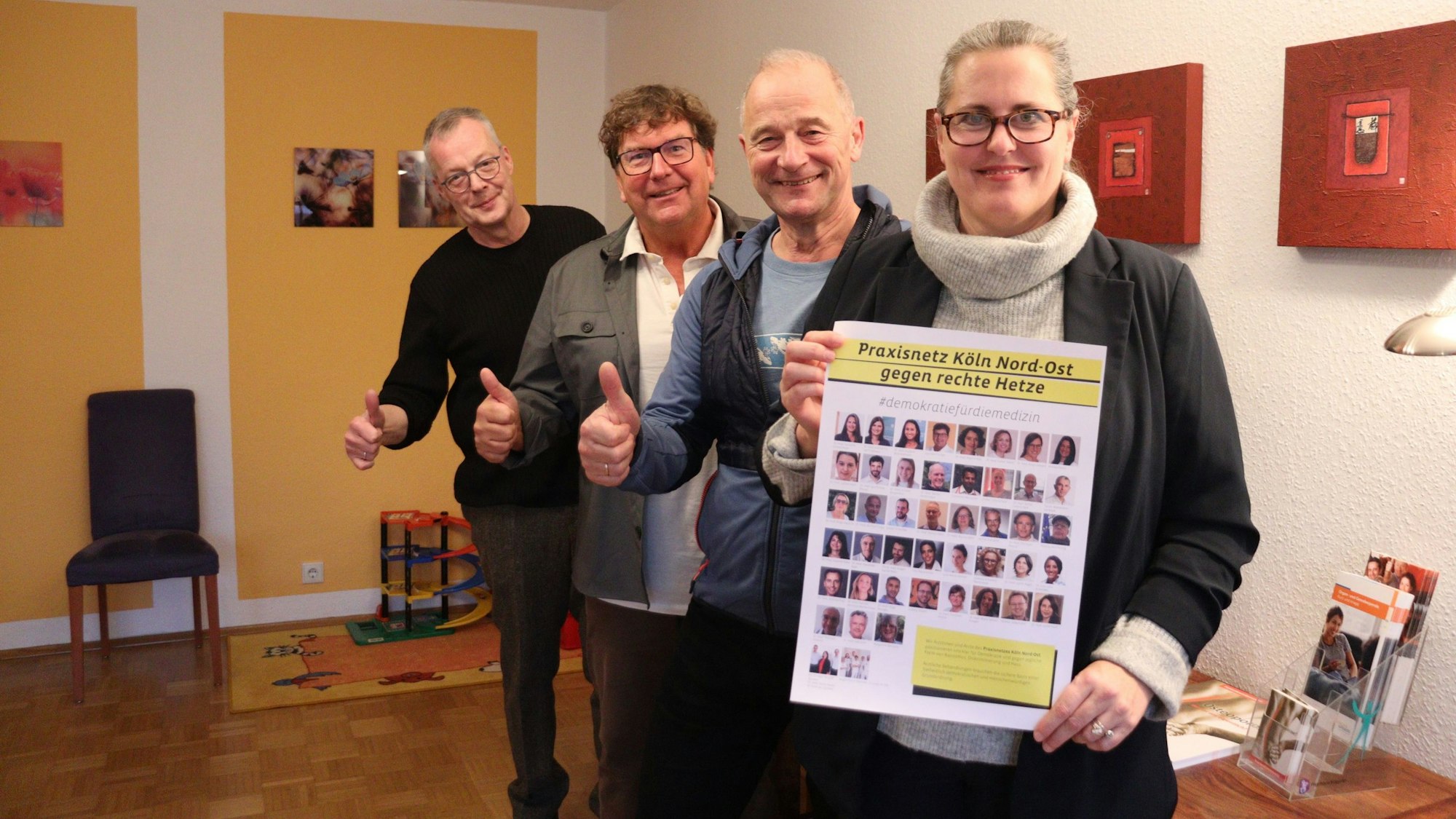 Eine Frau steht vor drei Männern. Sie hält ein Plakat mit Porträt-Bildern hoch.
