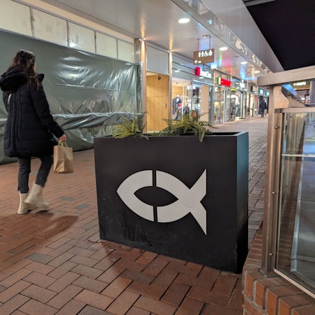 Ein Blumenkasten mit Fischsymbol vor der mit Plastikplanen verhüllten, geschlossenen Nordsee-Filiale.