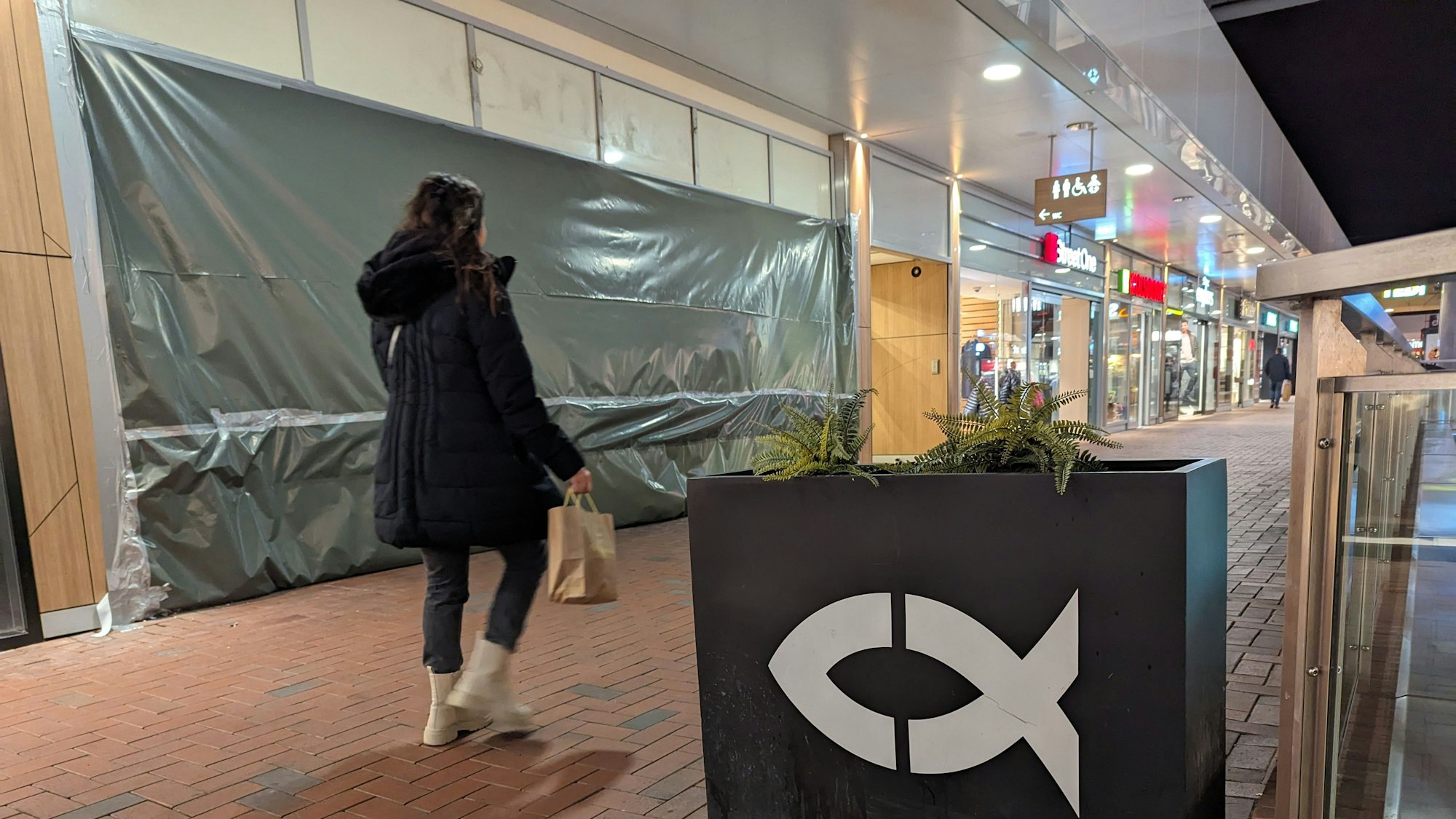 Ein Blumenkasten mit Fischsymbol vor der mit Plastikplanen verhüllten, geschlossenen Nordsee-Filiale.