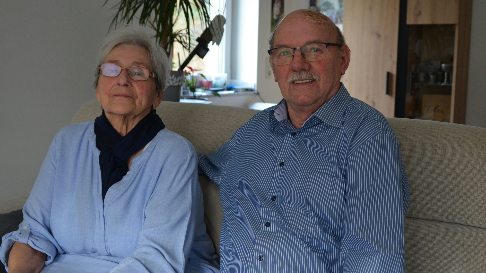 Dorothea und Klaus Scheurer sitzen auf dem Sofa in ihrem Wohnzimmer.