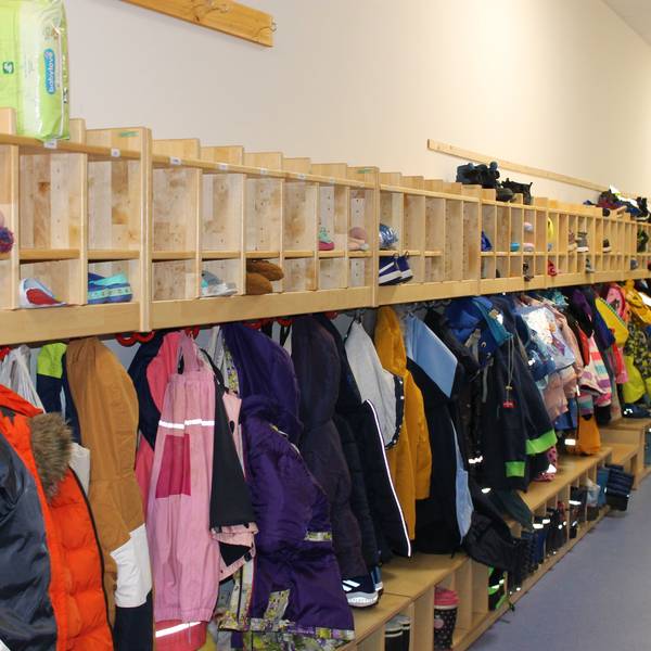 Das Bild zeigt eine Kita-Garderobe, an der viele bunte Jacken hängen.
