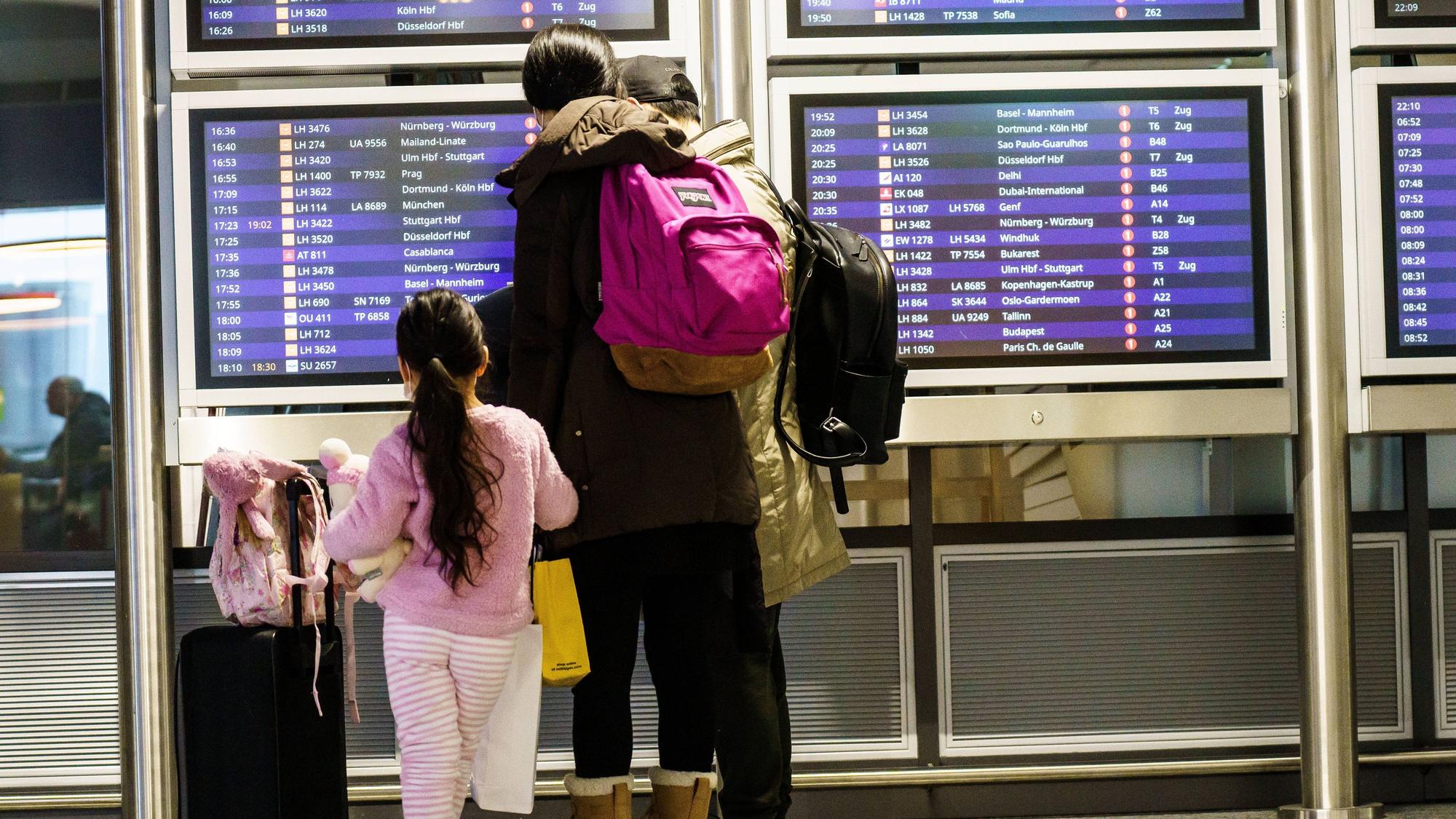 Eine Familie steht an der Anzeigetafel an einem Bahnhof.