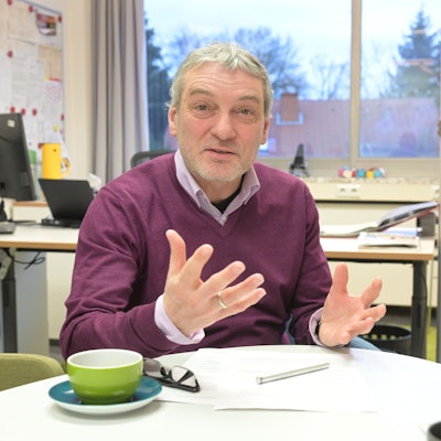 Herr Nagel sitzt an einem Tisch in seinem Büro. Auf dem Tisch liegt seine Brille, daneben steht eine Kaffeetasse.