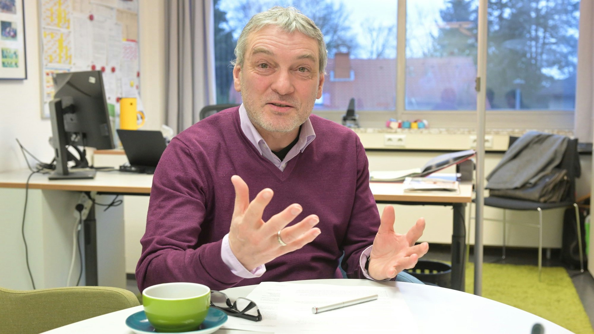 Herr Nagel sitzt an einem Tisch in seinem Büro. Auf dem Tisch liegt seine Brille, daneben steht eine Kaffeetasse.