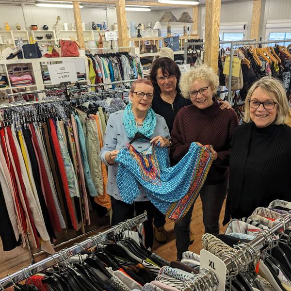Vier Frauen zeigen ein Kleid zwischen Regalen und Kleiderständern im Gewandhaus.