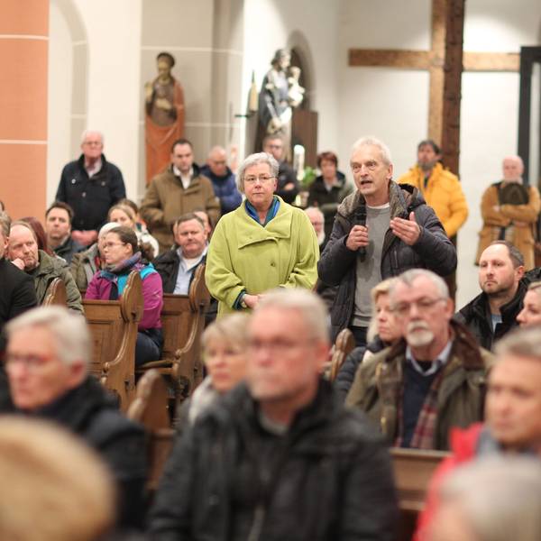 In einer voll besetzen Kirche steht ein Mann und spricht in ein Mikrofon.