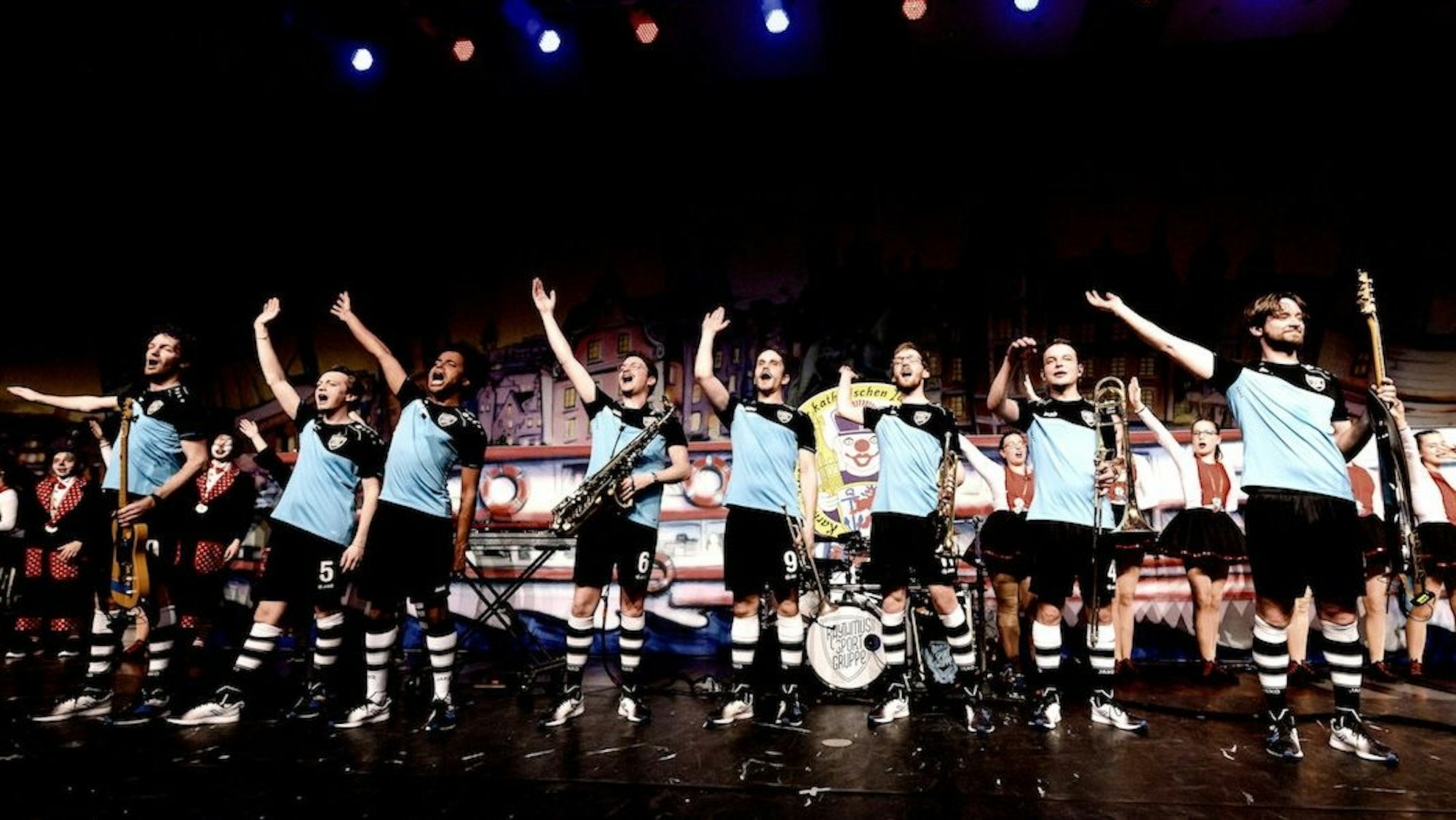 Die Rhythmussportgruppe stehen in türkisfarbenen Trikots zu neunt auf der Bühne.