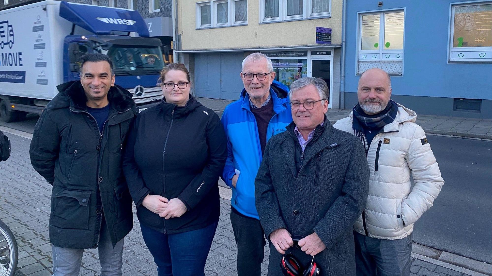 Zu sehen ist eine Gruppe von Bürgern vor der Heinrich-Esser-Straße, die gerade von einem Lkw befahren wird.